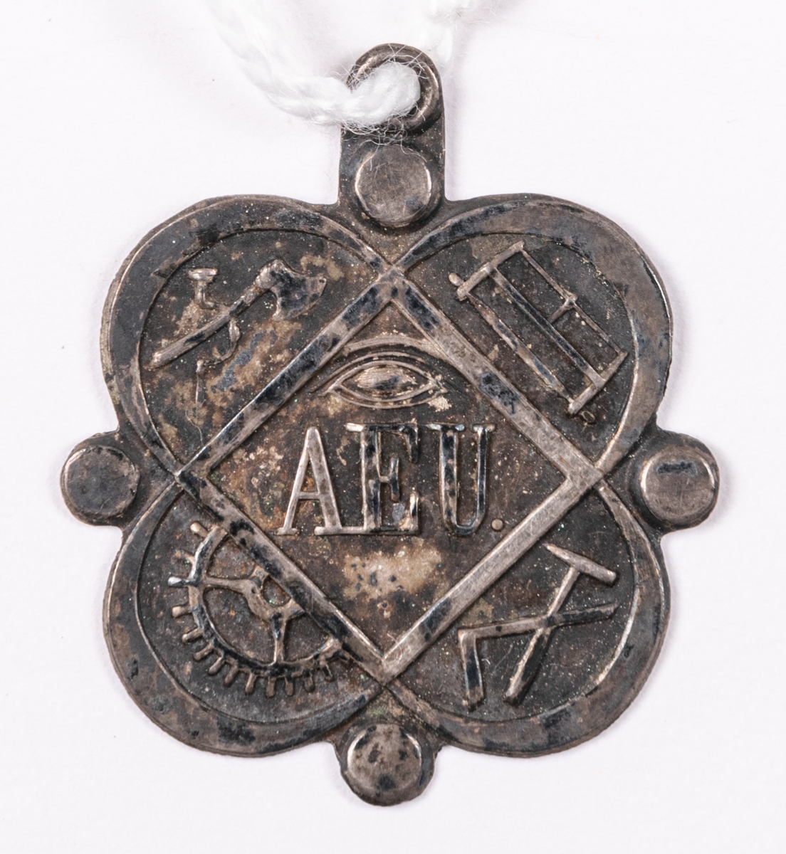 Föreningestecken i pressat silver, för okänt sällskap. Med emblem för olika hantverk, så som yxa, såg, hammare, vinkelhake och kugghjul, samt AEU.