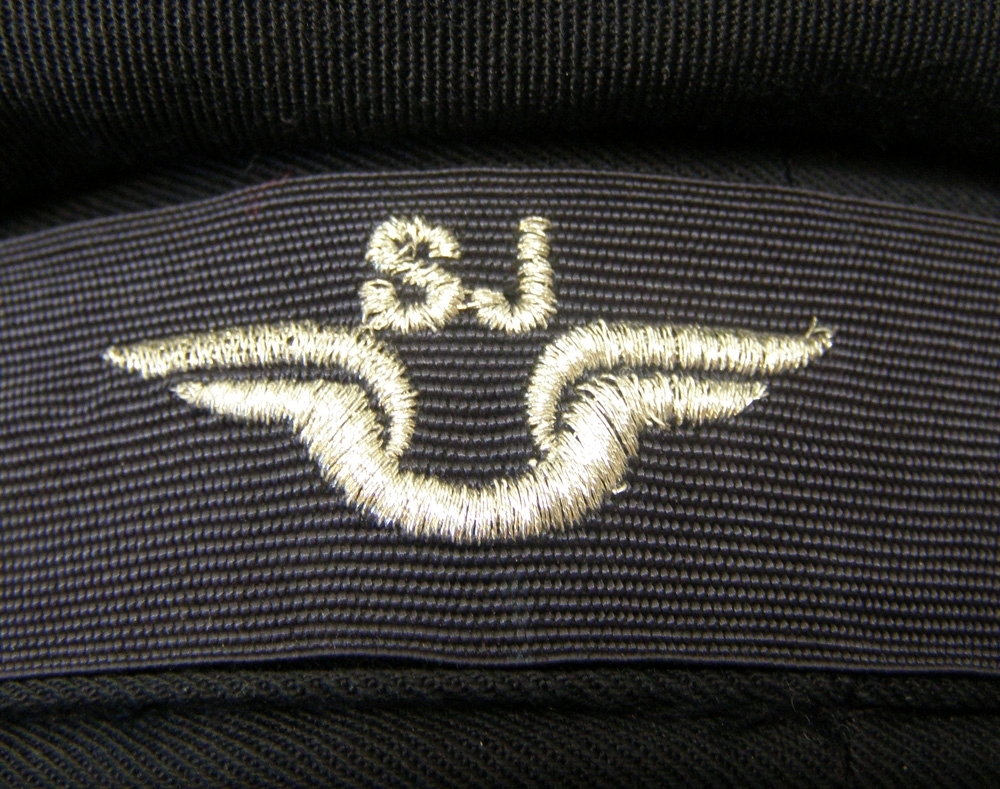 Märkblå basker av sommartyg. Mitt fram på mössan står SJ:s logotyp broderat i silver på ett mörkblått mössband.
Storlek 57.