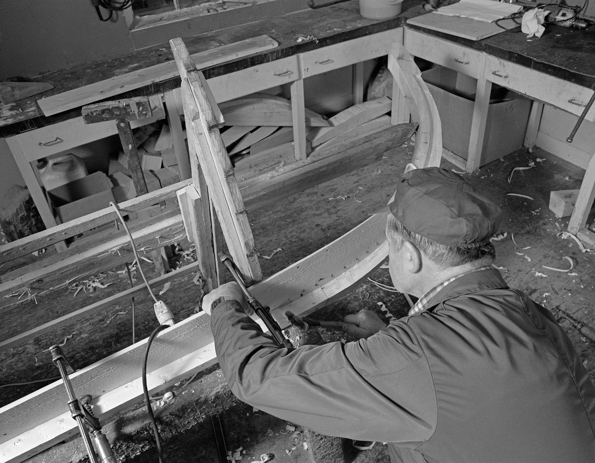 Bygging av fløterbåt i Glomma fellesfløtingsforenings verksted Breidablikk ved kommunesenteret Flisa i Åsnes i november 1984. Båttypen ble for øvrig kalt «Flisabåt», men denne modellen var egentlig utviklet av John Dybendal (1904-1985) omkring 1930. Målet var å kunne levere en robåt som passet i elva Flisa. Dybendal bygde sjøl slike båter fram til 1949. Glomma fellesfløtingsforening hadde vært en viktig kunde hos Dybendal, og da han gav seg som båtbygger ble virksomheten flyttet til denne virksomhetens verksted for Solør-regionen, hvor båtbygging ble vinteraktivitet for et par av karene som hadde vassdraget som arbeidsplass sommerstid. Det var maler til alle båtdeler, og skroget ble bygd på tverrmaler som ble festet til kjølen. Dette var hjelpemidler som gjorde det mulig for fløtere med reletivt liten håndverkserfaring å bygge denne båttrypen og oppnå den standardiserte formen som fløterkameratene var vant med. De fleste flisabåtene fikk jernspanter, for det var krevende å finne de krokvokste emnene som gav de beste spantene. Da Norsk Skogbruksmuseum dokumenterte båtbygginga ville karene likevel bruke trespanter. Da dette fotografiet ble tatt løsnet Lars Bernhard Olastuen (1927-1998) ei av tvingene han hadde brukt til å feste den første bordgangen til spankmalene før han spikret den fast til kjølen. Flisabåtene ble, som dette bildet viser, bygd løst. Kjølen var ikke fastspent i verkstedet, og den utferdige båten kunne dermed vippes fra side til side slik det passet under ulike faser i arbeidet.

Båten som var under bygging da dette fotografiet ble tatt ble seinere overlatt til Norsk Skogbruksmuseum, der den fikk nummer SJF.07823 i gjenstandssamlinga. Den er 518 centimeter lang og 153 centimeter bred. Odd Jensen har seinere lagd oppmålingstegninger, som også finnes i museets arkiv.