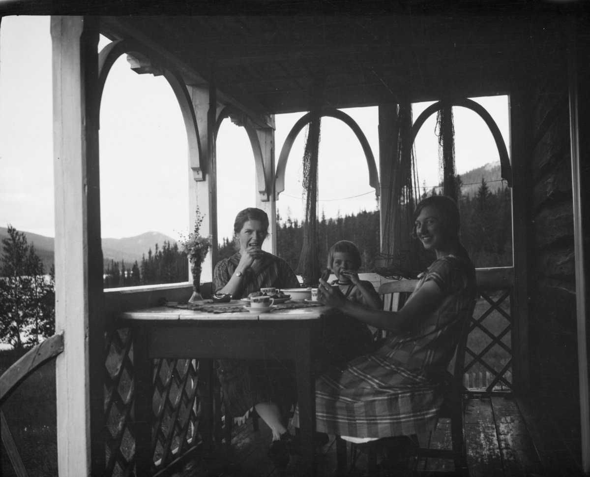 To kvinner og en jente ved kaffebordet på en veranda