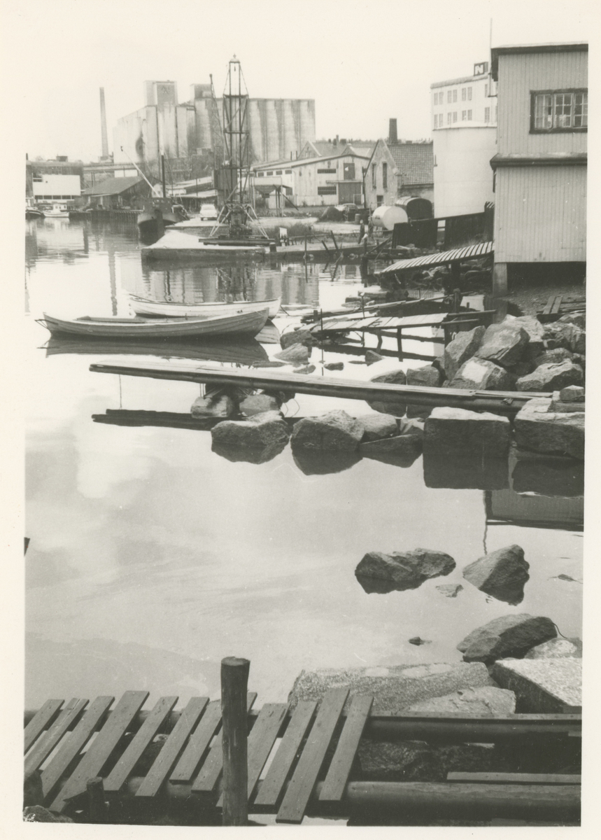 Mossesundet.

Fotograf har stått ved Sundbrygga.
Detaljer:	Moss Aktiemøller, lagerbygg, kran, små brygger, små båter, en del av Moss Roklubb til høyre.
Historikk: Fra 1950-tallet og utover forsvant alt vedlikehold av de gamle bryggene som falt fra hverandre.