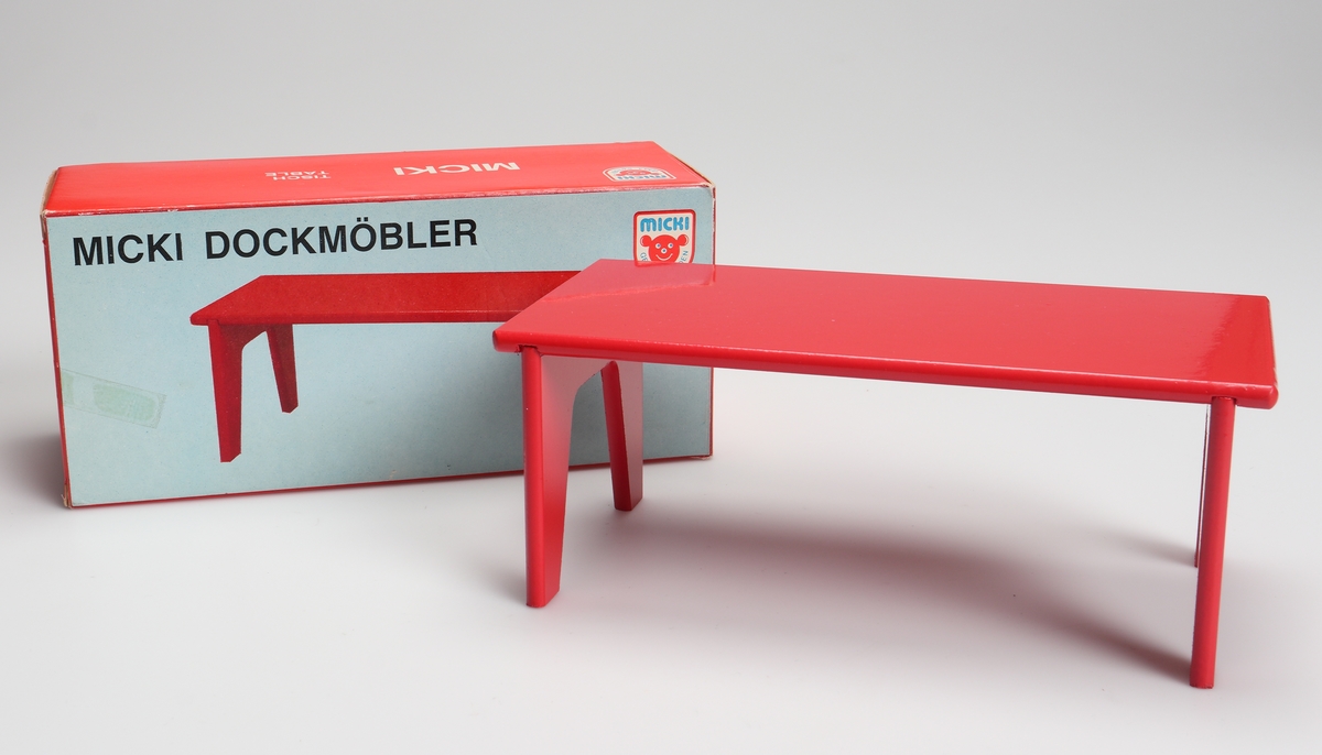 Rödlackerat bord (dockmöbel) tillverkad av träfiberskiva. Bordet har två benbockar fastlimmade i spår på skivans undersida. Bordet är förpackat i en röd och vit pappkartong med text på svenska, tyska, engelska och franska.

Inskrivet i huvudkatalog 1982.