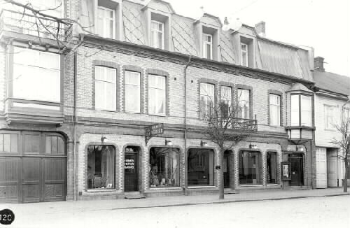 1906 lät sadelmakare E Malmgren uppföra huset. I vindsvåningen hade Sia Dahlbergs sin fotoateljé med fönster åt gatan. (Häftet kv. Kyrkan. Prästgården med flera).  På affärsskylten kan man läsa A/B Malmgrensmöbler, Foto Ateljér.