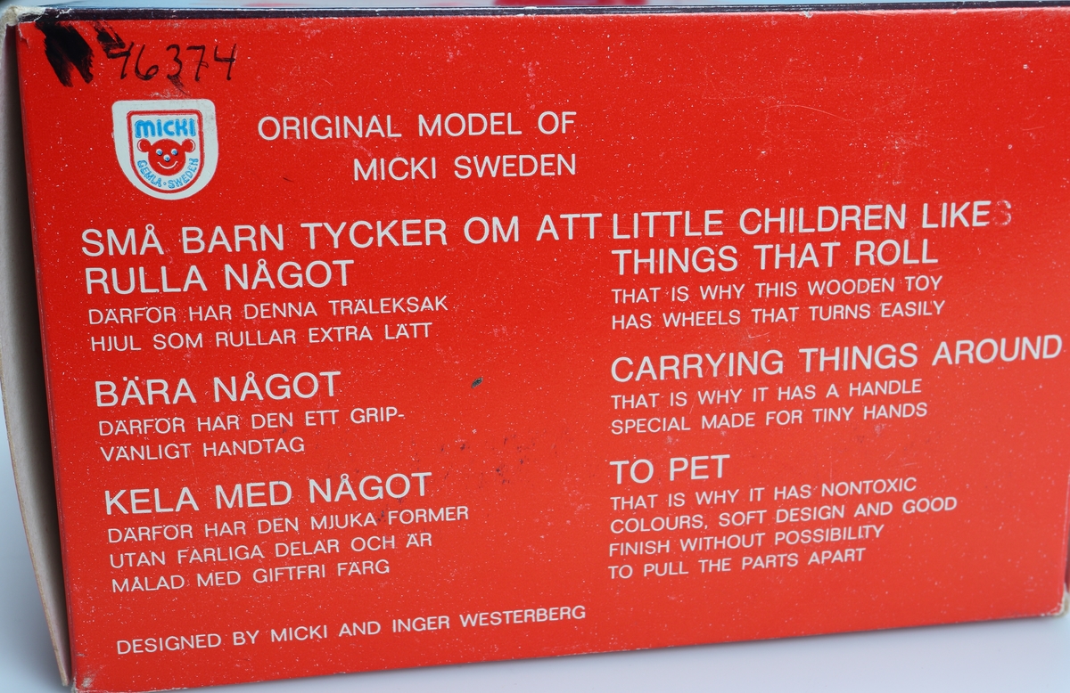 Rödlackerad leksakshund på fyra hjul. Ryggen är utformad som ett handtag. Hjulen är lackerade i orange färg. Morrhåren är gjorda av plast. Design: Inger Westerberg. Den är förpackad i en röd och blå pappkartong med bild och text på tyska, engelska och svenska.

Inskrivet i huvudkatalog 1982.