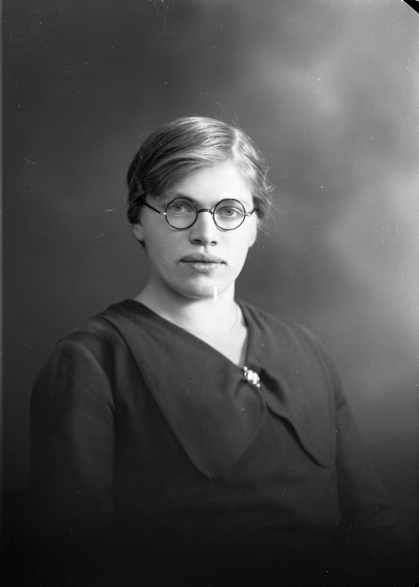 Porträtt av Elsa Karlsson, en ung kvinna med glasögon.