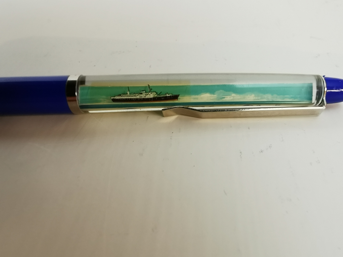 Plastikk penn med modell av M/S "Kong Olav" flytende frem og tilbake inne i pennskaftet. Metall hempe for å feste i pennen til eventuelt en lomme. Nede på pennen kan du skru pennspissen ut og inn.
