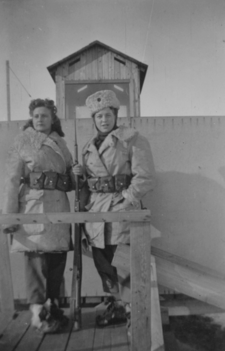 Porträttfoto av två kvinnliga luftbevakare stående i ett luftbevakningstorn vintertid, 1942. Klädda i uniform och med gevär. Till vänster Birgit Johansson, till höger Karin Nordberg. Luftbevakarna tillhörde 91:a ls-kompaniet i Tellejåkk, Kåbdalis under beredskapsåren.