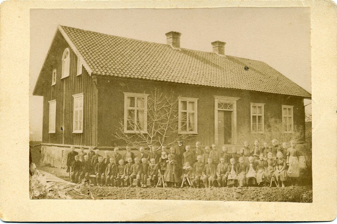 En skolklass sitter och står framför Uppgränna skola tillsammans med läraren J Mellin.