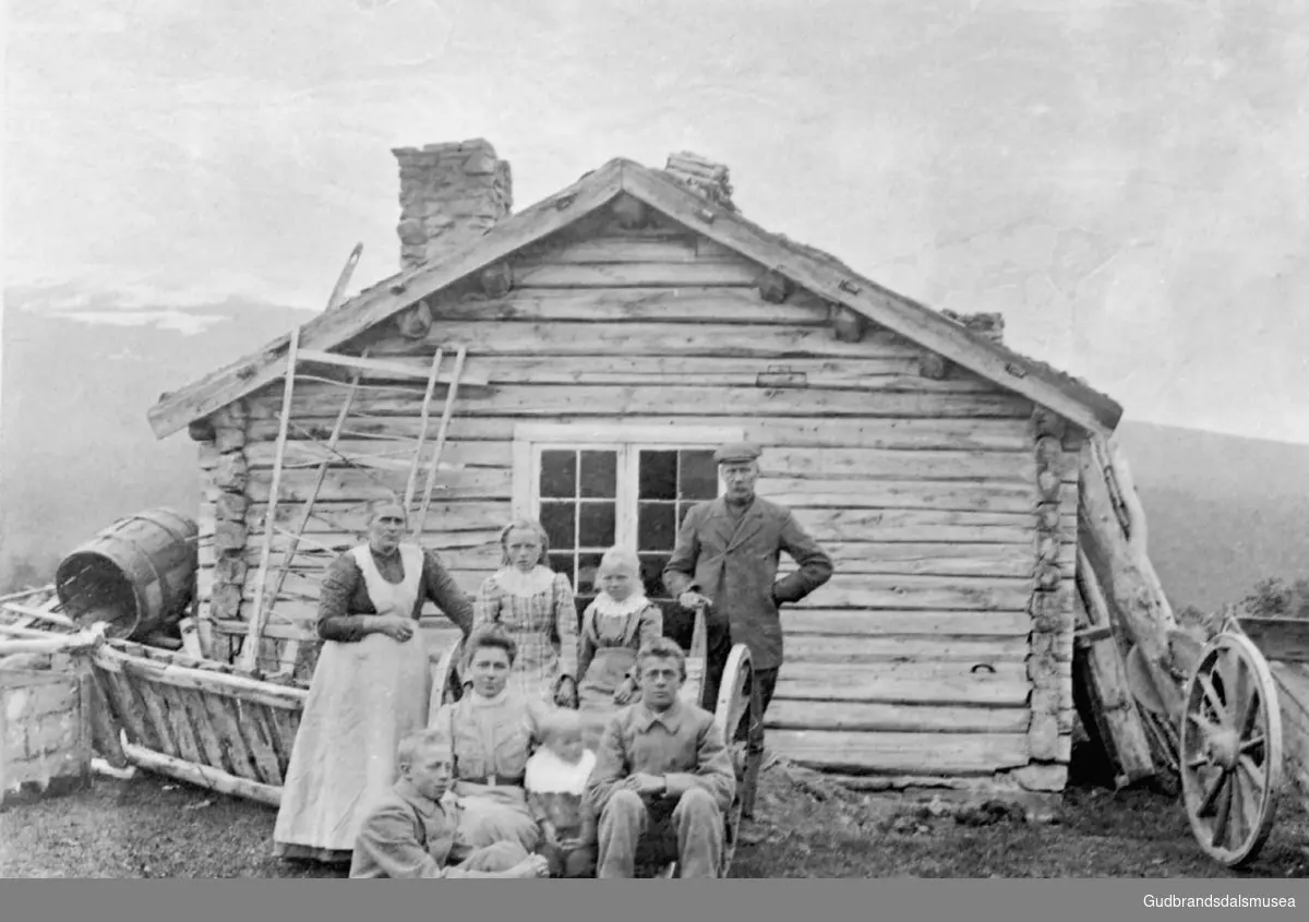 Ola og Marit Mølmen og ungane, ved eit av husa i Mølme?, åtte personer foran en mindre bygning, seks av dem sitter på en kjerre.