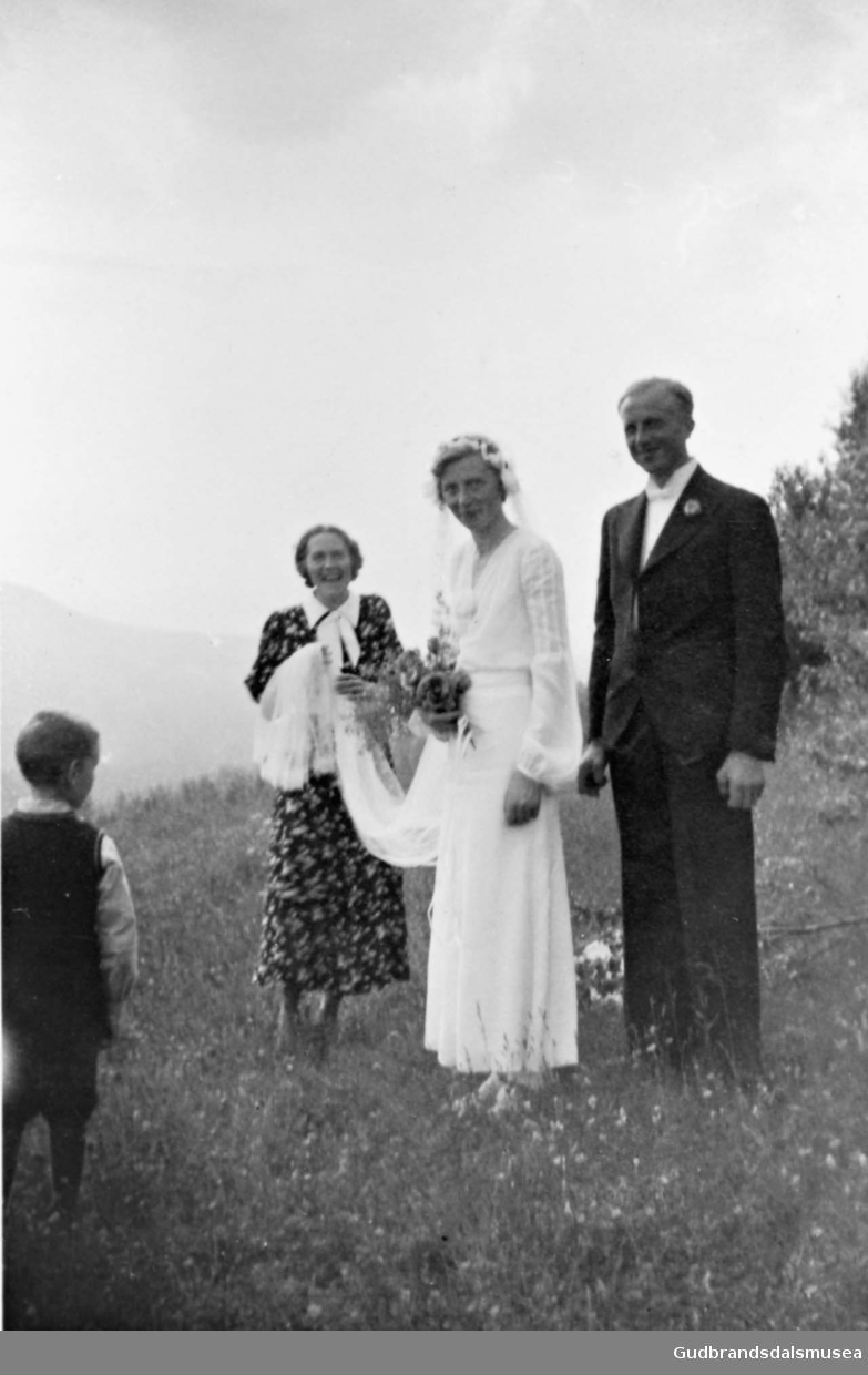 Portrett, brudeparet fotografert ute på jordet på Nørdre Plassen, kvinne og gutt står rundt.

