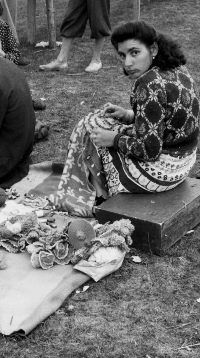 Romsk kvinna virkar på Kiviks marknad 1947. Hon virkar minnessaker till försäljning.