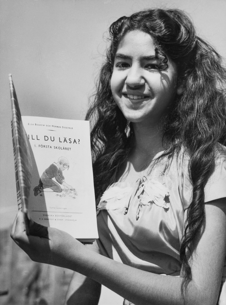 En romsk flicka håller upp sin läsebok i ett läger i Malmö 1955.