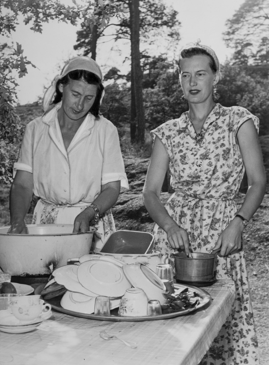 Två kvinnor står vid ett bord utomhus och arbetar med disken. I bakgrunden syns träd. Kvinnan till höger är gift med en svensk-romsk man men hon själv är inte rom. Äktenskap mellan romer och icke-romer har dock inte varit ovanligt genom historien.