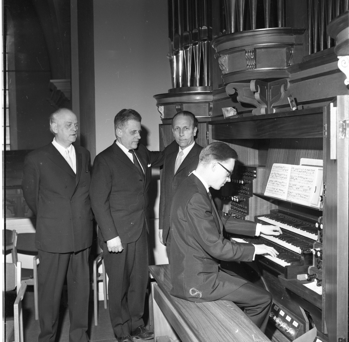 Fyra kostymklädda män vid Gränna kyrkas nya orgel, till vänster står musikdirektör Sture Petri. Den yngre av dem sitter och spelar.