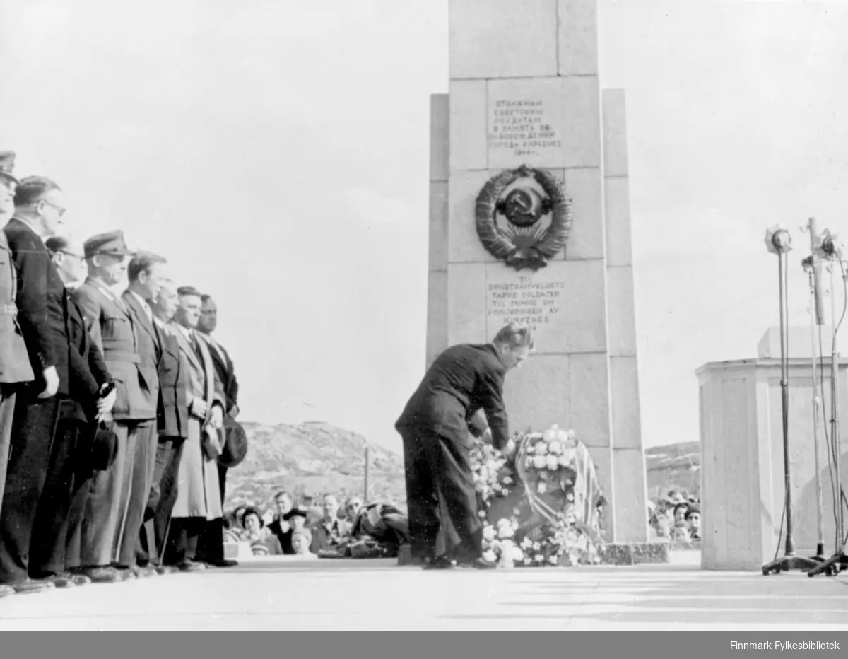 Nedlegging av blomster på russemonumentet i Kirkenes, 8.juni 1952. Monumentet ble reist til Sovjetsamveldets tapre soldater til minne om frigjøringa av Kirkenes 1944. En mann legger ned blomster mens flere menn står til venstre og følger med.