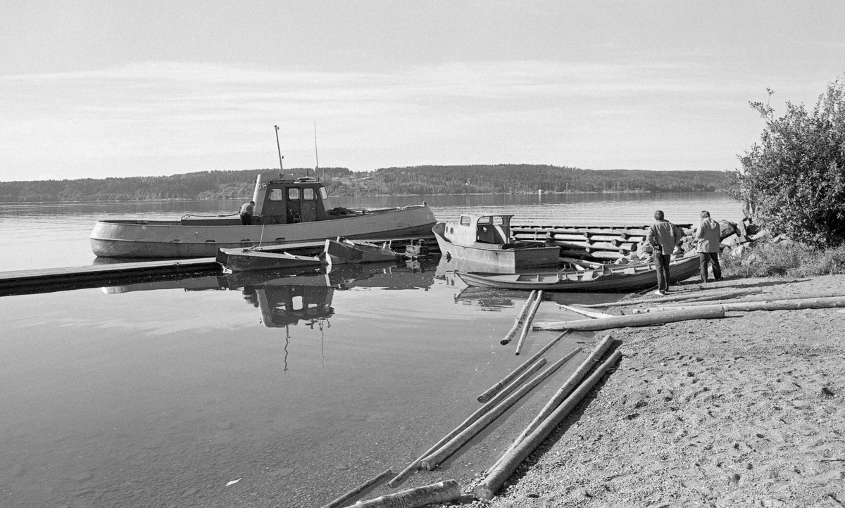 Fra brygga på Sandstangen i innsjøen Øyeren i Trøgstad i Østfold.  Da dette fotografiet ble tatt lå det to båter ved brygga, som var en tømmerkonstruksjon.  Den største av dem er «Vister», en liten slepebåt, omtrent på størrelse med Rauma, som gikk i lenseområdet ved Fetsund i nordenden av sjøen.  Den andre båten på fotografiet, som også har jernskrog, er en varpebåt med førerhus forut og en trommel akterut.  Slike båter ble brukt under oppsamling av løstømmer i bommer på innsjøen.  Slike bommer ble bundet til de store slepene slepebåten Mørkfos trakk mellom Fetsund lenser og Sleppetangen, hvor Glomma forlater Øyeren.  Mot den sandete strandbredden, innerst ved brygga, ligger en klinkbygd robåt.  Utenfor, foran Vister, synes det å ligge en fjerde farkost delvis nedsenket i vannet.  Sandstangen ligger rett overfor Sleppetangen i Spydeberg, på motsatt side av innsjøen, der nedre del av Glomma rant ut av Øyeren.  På dette stedet er innsjøen, som fotografiet viser, forholdsvis smal.  I noen tilfeller ble tømmerslepene lagt på Sandstangen i stedet for ved Sleppetangen på vestsida av Øyeren.  Dette skjedde imidlertid ikke ofte.

Etter den siste fløtingssesongen i Glomma, 1985, overdro Glomma fellesfløtingsforening eiendommen Sandstangen med båthus, kvilerom, lagerhus, smie og oljetank til Trøgstad kommune.