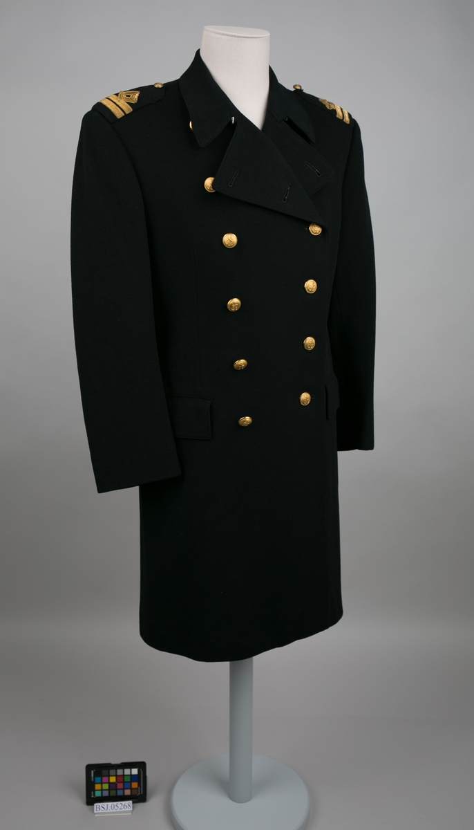 Førstestyrmann uniformsfrakk med distinksjoner på hver skulderputer. Dobbelspent med til sammen 12 stk. knapper i gullfarge med motiv av anker (en mangler).