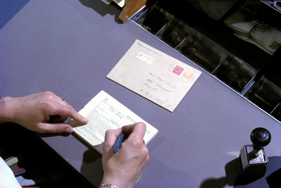 Seriebild H 7. En postkassör på poststationen Bromma 12 skriver ut
ett kvitto på inlämnat rekommenderat brev, som är frankerat
ochförsett med en rek-etikett. T h står en stativstämpel.