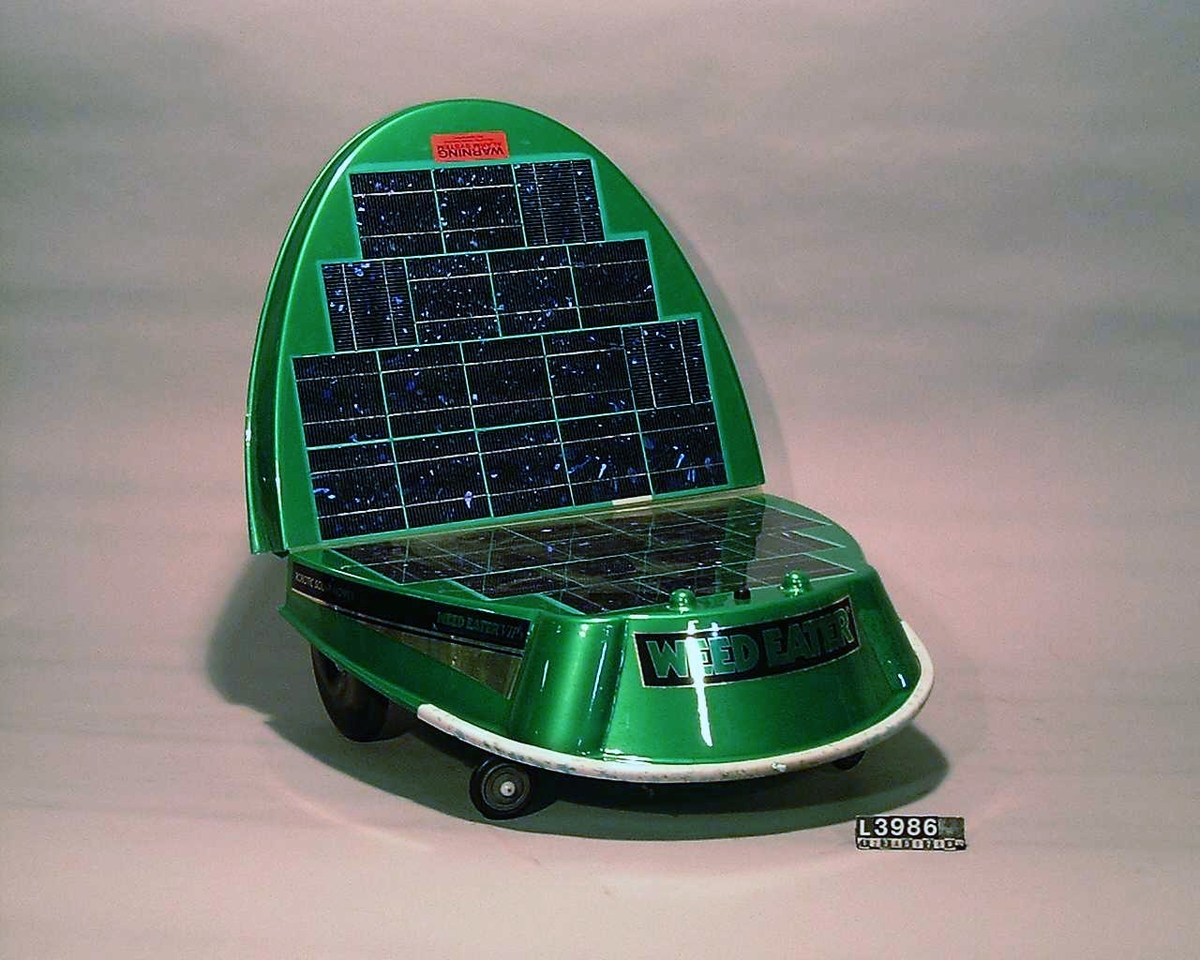 Robotic solar mower. Självgående gräsklippare som drivs med solceller. Gräsklipparen är oval till formen, grönmålad och på ovandelen sitter solcellerna. Formen på gräsklipparen påminner om en skalbagge/gräshoppa.