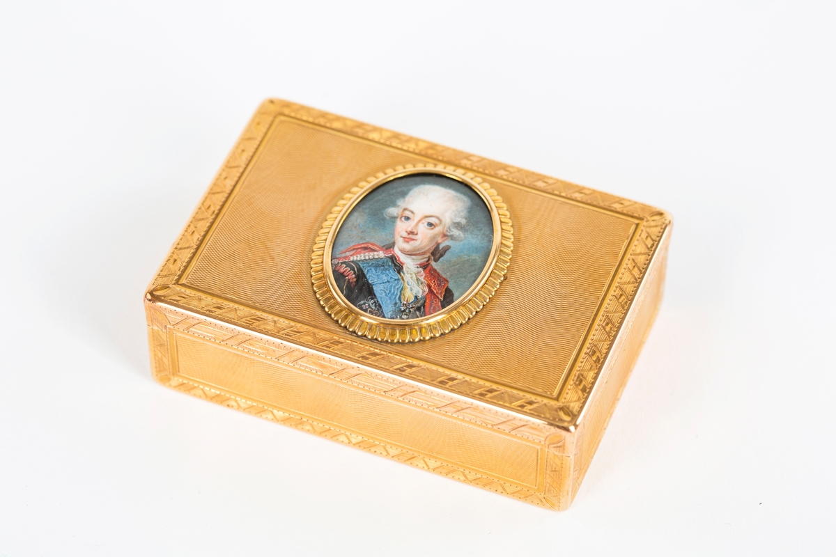 Rektangulär snusdosa av 18K guld. 
Moiregraverade ytor med graverade mönsterbårder. 
På locket medaljong med miniatyr föreställande Gustav III, målad av Lennard Örnbäck (1736 - 1789).
Ligger i en röd ask, ej från tiden.