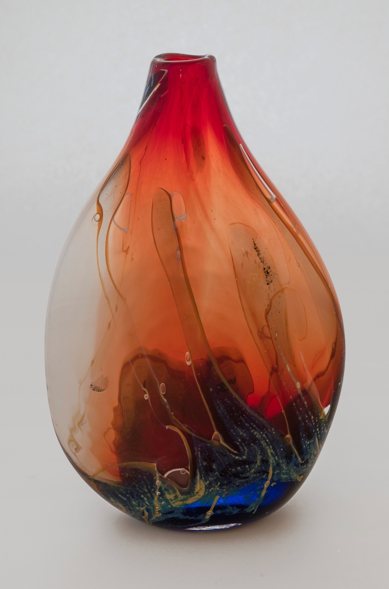 Flattrykket dråpeformet vase av farget glass. Korpus er rødbrunt med glidende fargeskiftninger i blått, hvitt og grønt. En del luftblærer i glassmasssen.