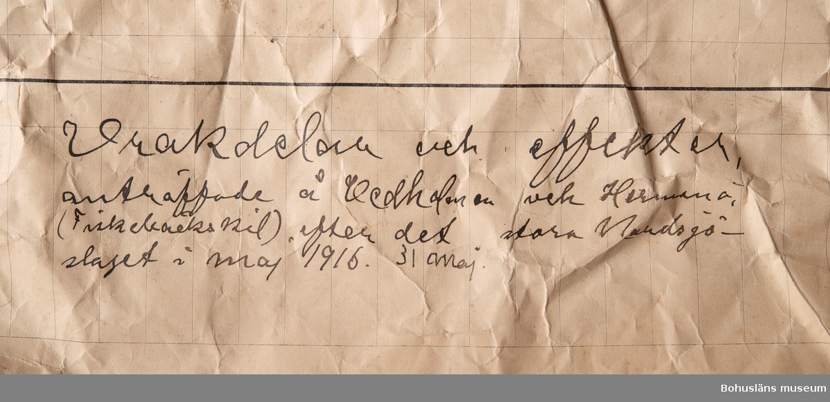 Rund uniformsknapp av gulmetall med gjutet motiv av krönt ankare. 
Vidhängande handskriven etikett med text:
"Tillhört engelsk sjöofficer, se protokoll vid polisundersökning den 22 Juni 1916 - No 11", skrivet av landsfiskal Erik Holst.
