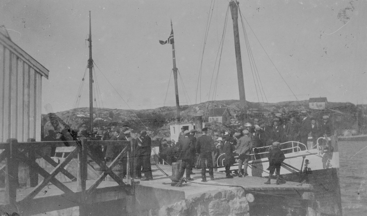 Bildet viser en båt som ligger ved kaia på Steinsjø, Kvenvær. Mange mennesker på kaia.