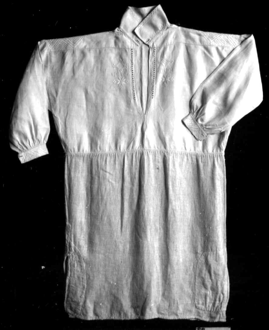 Bunadsskjorte av lin, med brodering og hullsøm på mansjetter, krage og stolpe. Nederste del av skjorten er av strie.