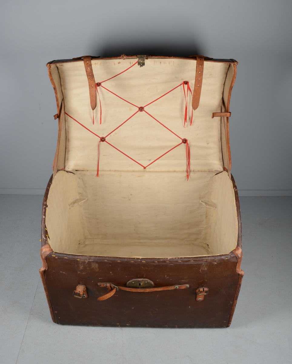 Koffert med lokk hengslet i to reimer som går over lokket og festes i to spenner. Defekt lås. Skroget er av kartong kledd i brunmalt tekstil. Innsiden foret.