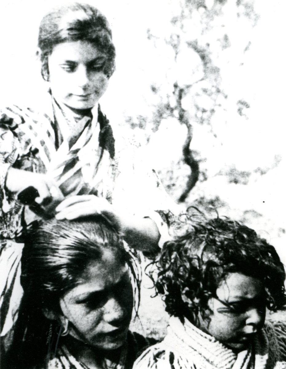 En ung kvinna kammar håret på en flicka framför henne. Bildens ursprung är okänt.
