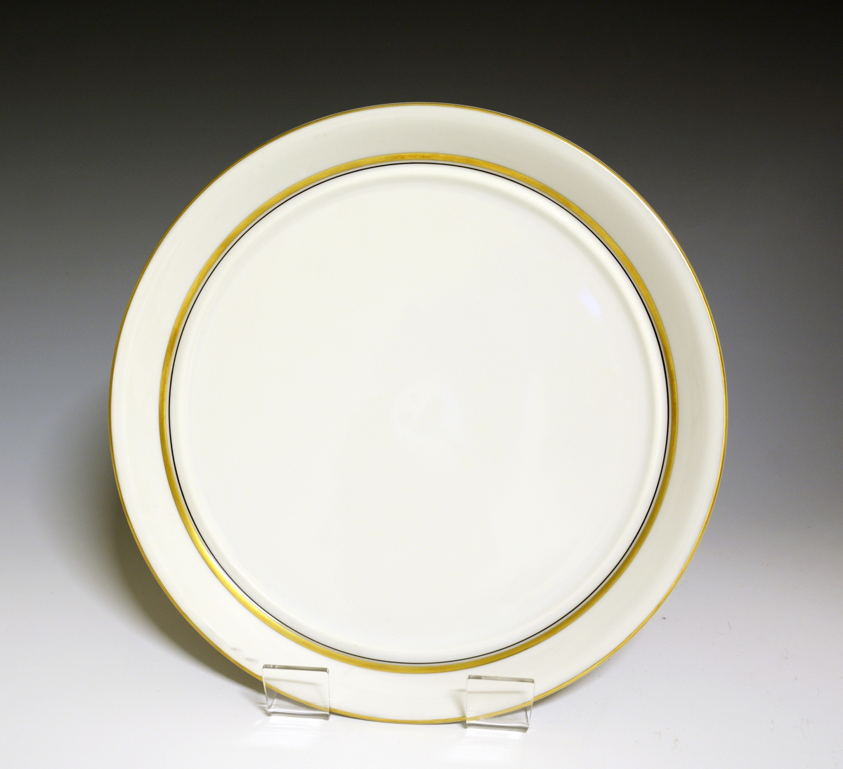 Tallerken av porselen med hvit glasur, gullstrek oppe og nede.
Modell: 2410 Marguerite. 
Dekor 50022 Spinett.