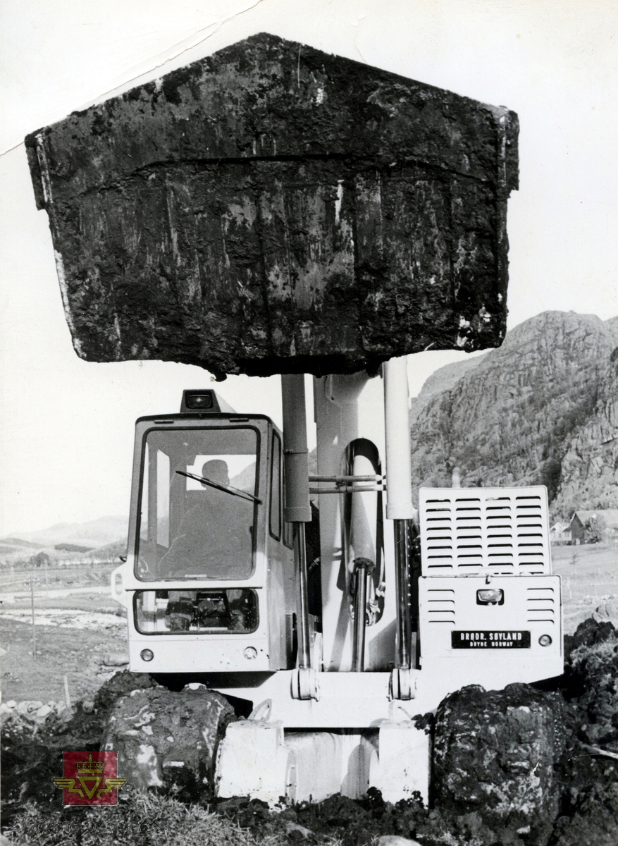 Brøyt X3, 1965 modell i arbeid på Europaveg 18-anlegget på Kyllingstad i Gjesdal kommune. 
Skilt på gravemaskinen: "Brød. Søyland Bryne Norway."
Bilde 2) Viser landskapet og gravemaskinen sett fra siden.