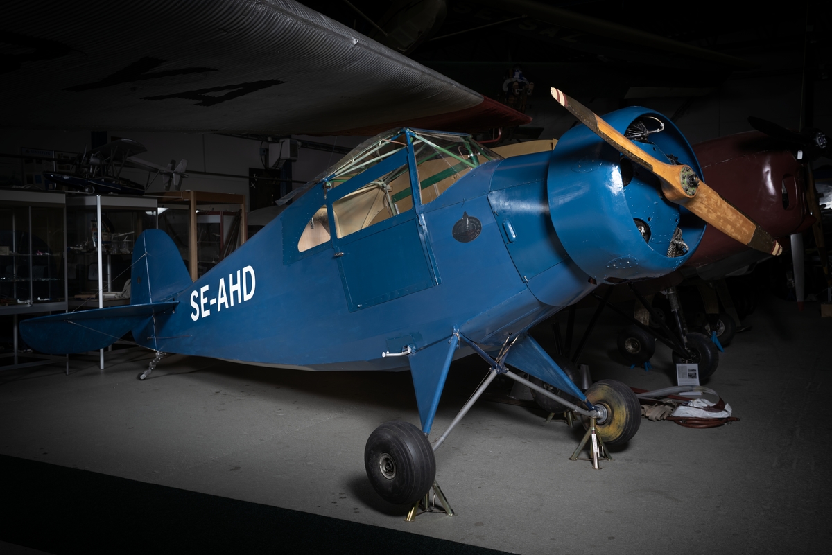 Flygplan av modell GV-38. Motorflygplan med täckt kabin och två sittplatser i tandem. Högvingat monoplan, blåmålat.
