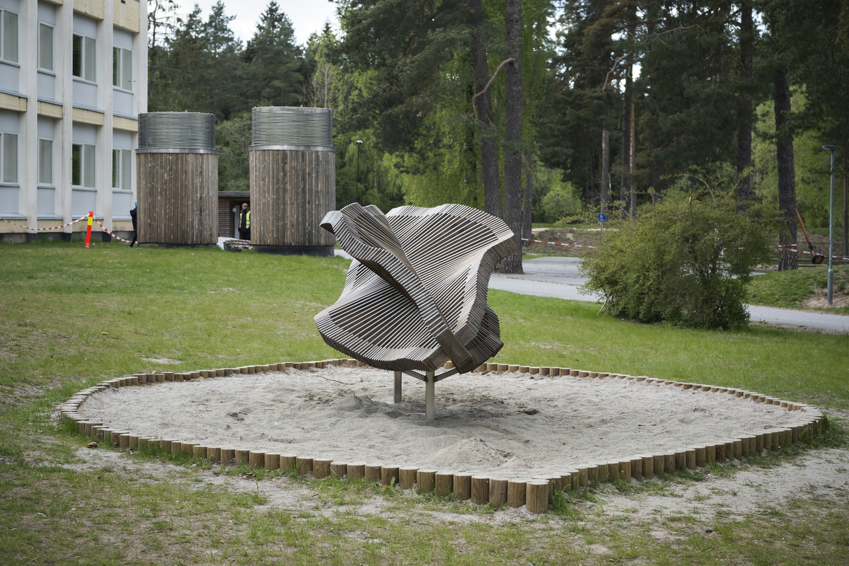 Skulptur utformet i tre. Skulpturen utgjør en flytende form bestående av trespiler. Plassert i skolens utemiljø blant grantrær foran nytt administrasjonsbygg. 