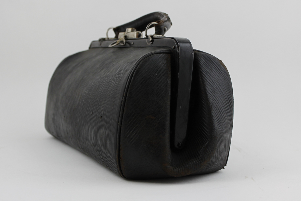 Väska av läder ovalformad försedd med knäpplås av nickel och handtag.