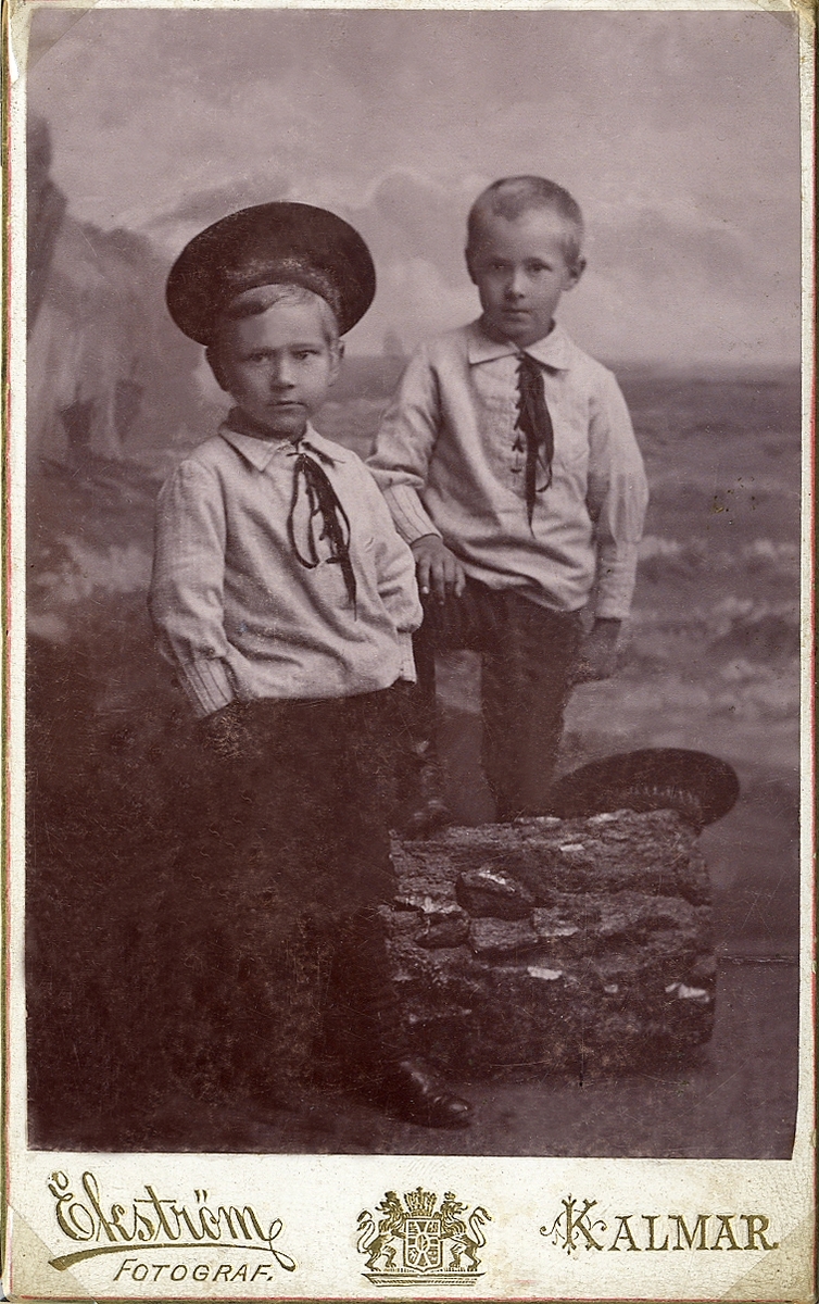 Porträttfoto av två pojkar i kortbyxor, bussaronger och sjömanshattar. 
Helfigur. Ateljéfoto.