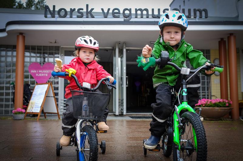 Bildet viser to barn på sykkel foran inngangen til Norsk vegmuseum.