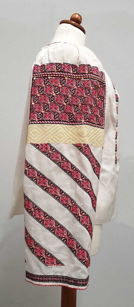 Hvit bluse av lett, nesten transparent bomull, med gullpaljetter og broderier i rødt, svart, gull og gult på bryst og ermer.