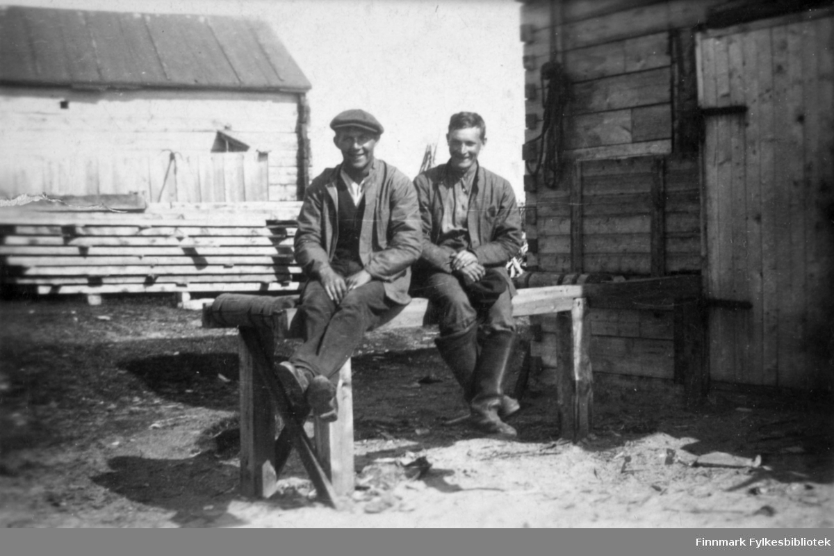 To menn sitter på bordet eller benken i Salttjern. I bakgrunnen ser vi mange planker stablet oppå hverandre.