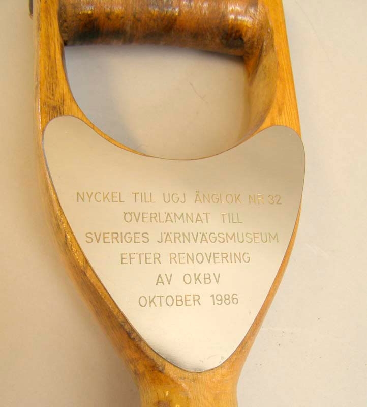 Kolskyffel av metall med träskaft. På skaftet står följande text inristat på en metallplatta:
"Nyckel till UGJ ånglok nr 32
överlämnat till
Sveriges Järnvägsmuseum
efter renovering 
av OKB
Oktober 1986"
