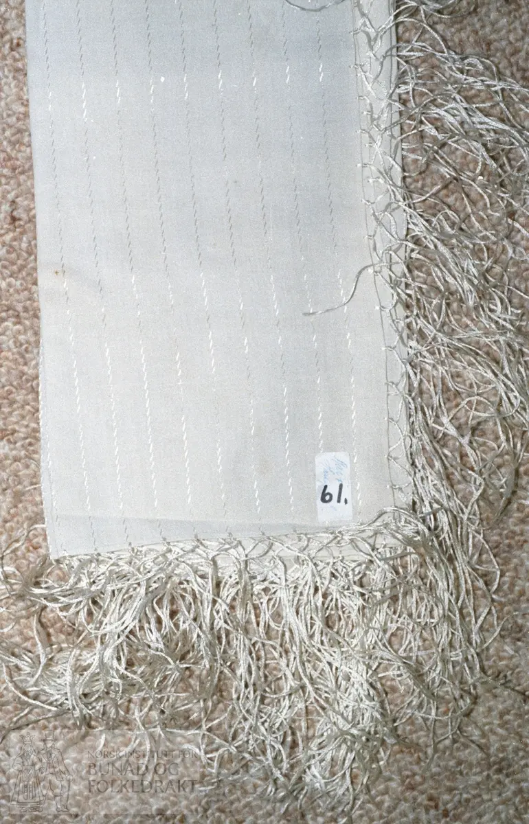 Småmønstra. gulkvit ull med striper i gulkvit silke. Silketafs i det same garnet. Tørkleet er truleg frå kring århundreskiftet.