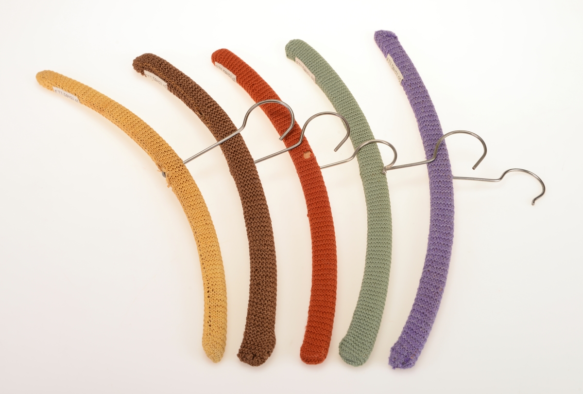 Fem enkle klesehengere laget av tre med strikket trekk. Trekkene er strikket i rettstrikk/rillestrikk. Det er strikket en remse som er sydd sammen på undersiden/langsiden av kleshengerne. Det er strikket i 5 ulike farger. For oppheng er det en enkel krok i metall.