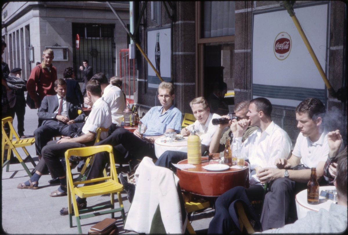 Menn drikker øl og fotograferer, ved uteservering langs gaten. 'Sagafjord' Spring Cruise to Europe 1966.