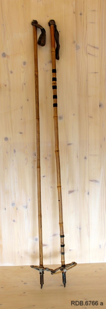 Et par skistaver laget av bambus. Fastklinkede håndhemper av lær øverst og trinser i bambus som holdes sammen med et kryss av skinnreimer som er klinket fast til staven. Den eine trinsa er kvit, den andre er grå (trolig utskiftet). Nederst på stavee er det: messingholker og jernpigger. Den ene staven er sprukket og sammenlimt med svart tape på to plasser.