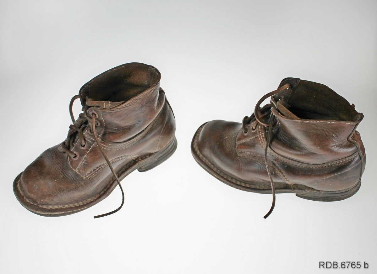 Et par brune barnesko laget av en bygdeskomaker. Skoene har åpning med tunge foran og lukkes med skolisser i lær tredd gjennom 5 par maljer. Skoene er randsydde. Det er slitt hull på sålen under venstre sko.