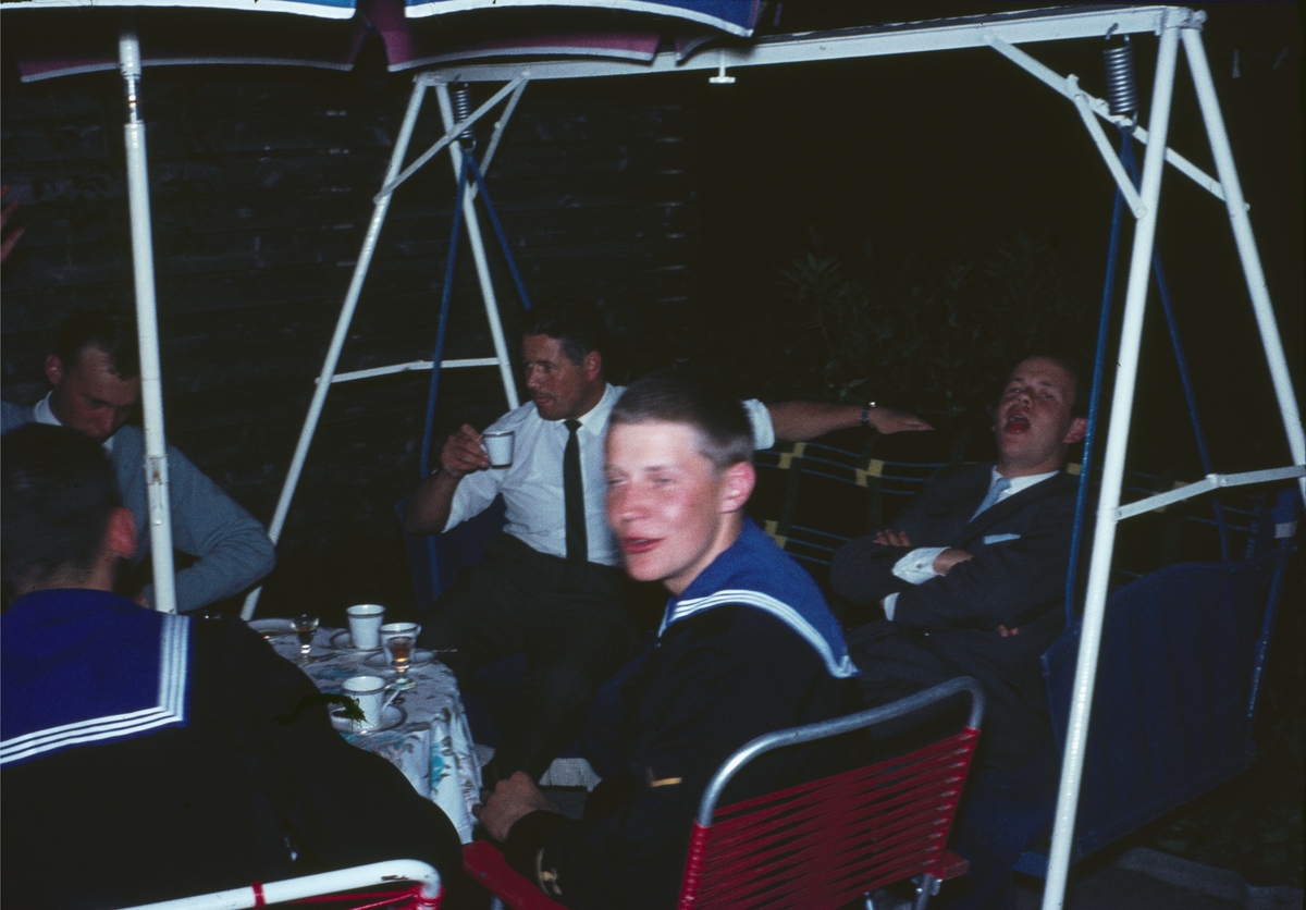 Bilden visar en grupp unga män dels i sjömanskostym dels i civila kläder som sitter runt ett bord och skämtar. Två at de sitter på en hammock.
