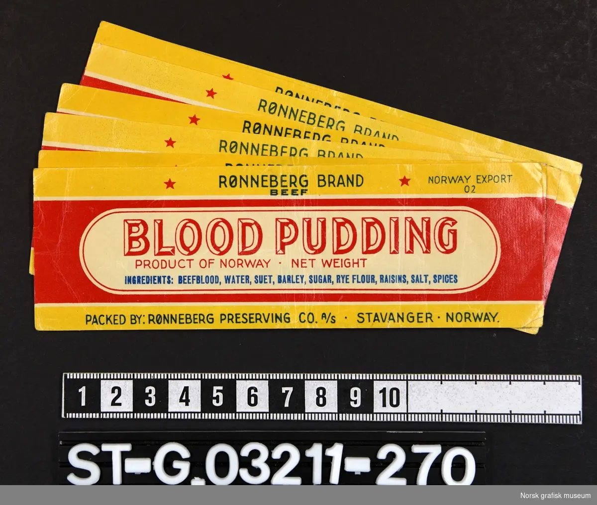 Etikett i rødt og gult, hvitt og blått, dominert av varebeskrivelsen i en hvit ramme. 

"Blood pudding"