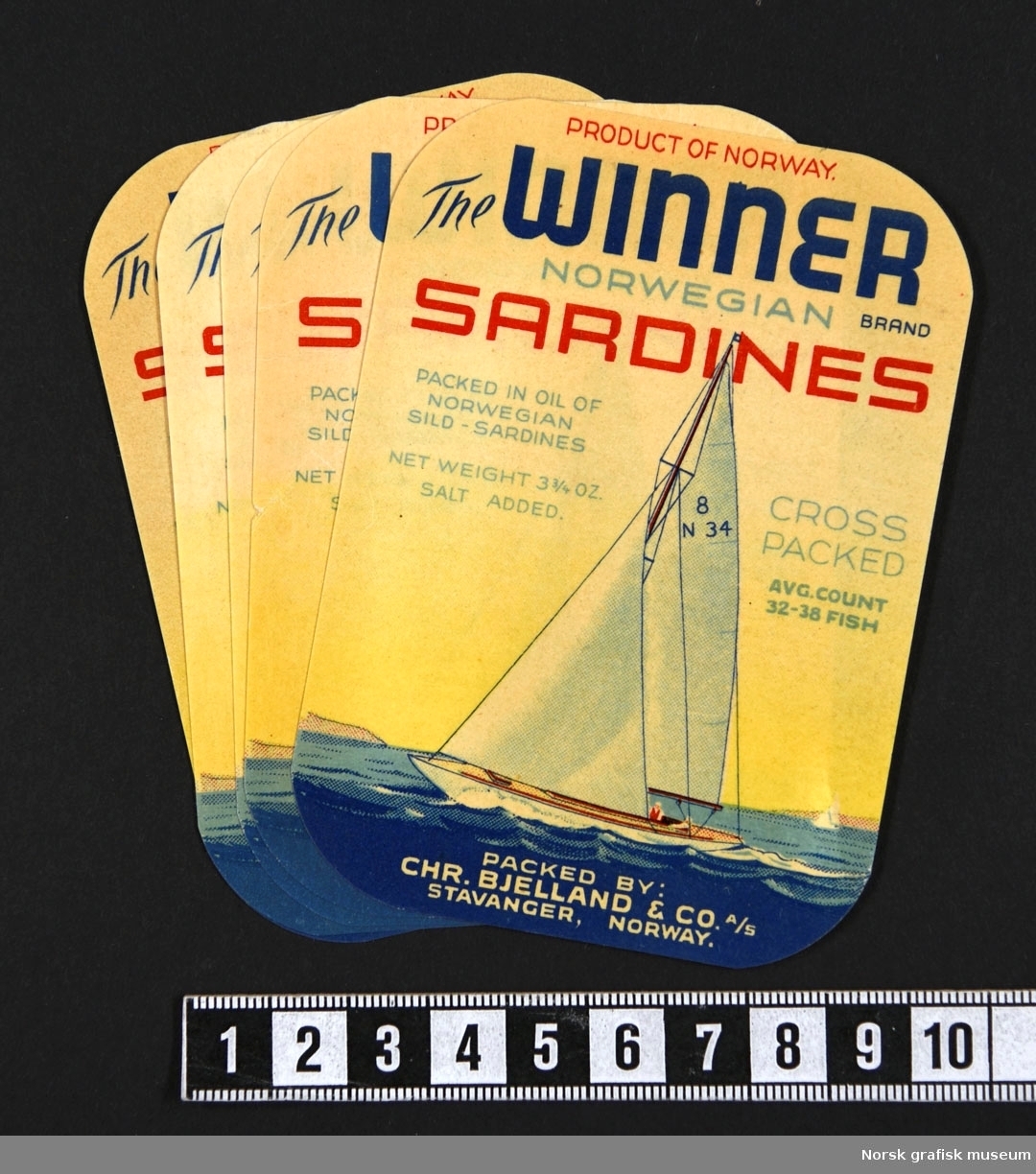 Etiketter med fremstilling av en seilbåt med hvite seil, på blått hav, under en gul himmel. 

"Sardines packed in oil of Norwegian sild- sardines"