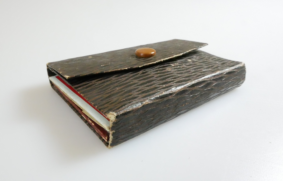 Rektangulær lommebok i brunt kartongmateriale. Deler av pappen kan brettes og festes med en knapp. Inne i lommeboken er det et speil og en lomme. 
