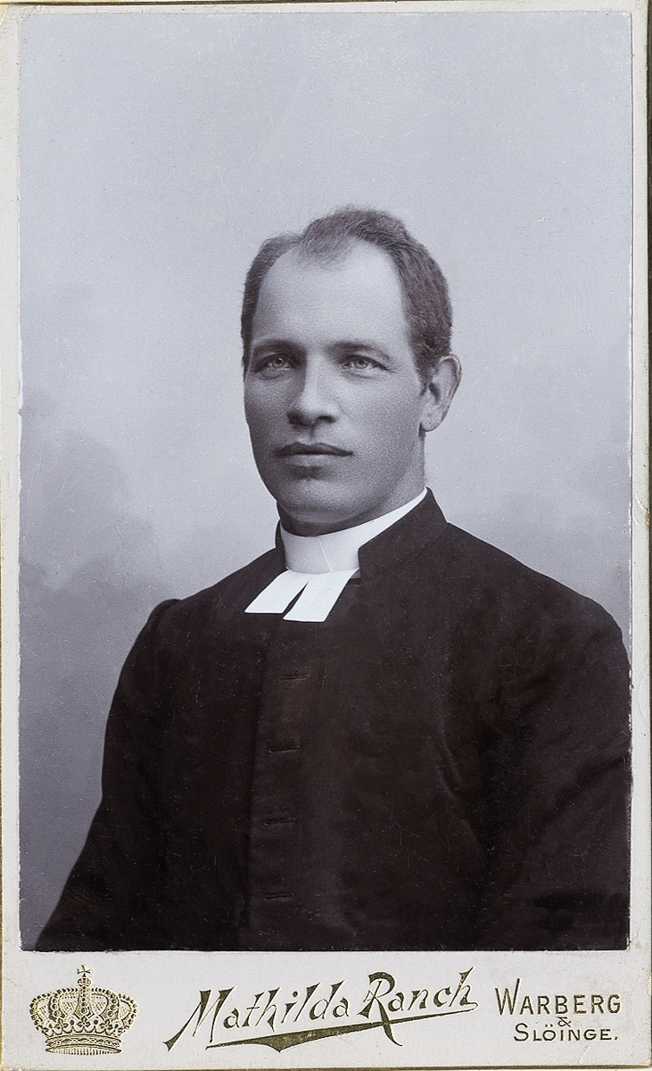 Foto av en man i prästrock med prästkrage m.m.
Bröstbild, halvprofil. Ateljéfoto.